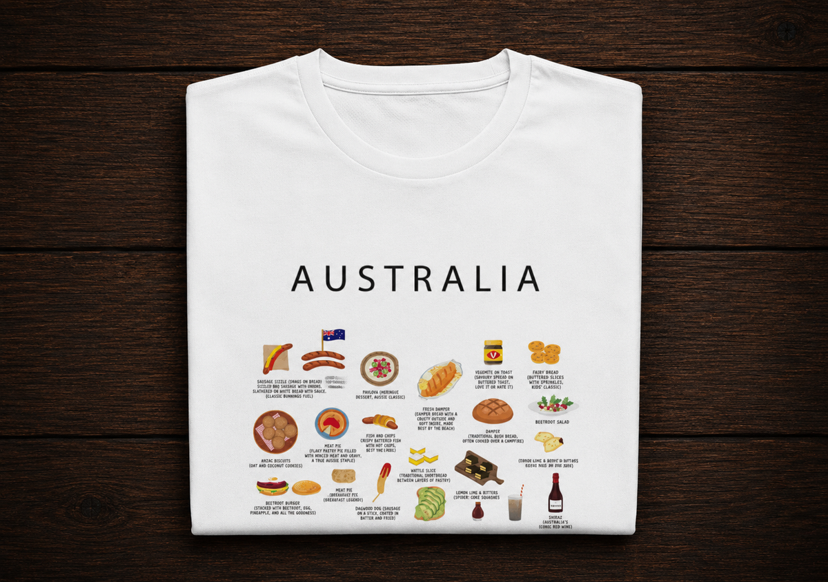 A white folded t-shirt with a graphic print of Australian food items and text under the word 'AUSTRALIA', displayed flat on a dark wood background.