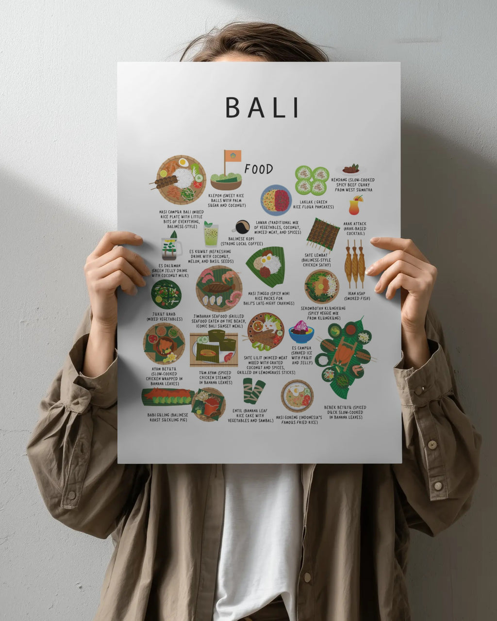 A person holds a white Bali food poster covering their face, featuring colourful illustrations and names of traditional Balinese dishes.