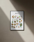 A black-framed Bali food poster displaying illustrated local dishes, hanging on a beige wall bathed in diagonal natural sunlight and shadow.