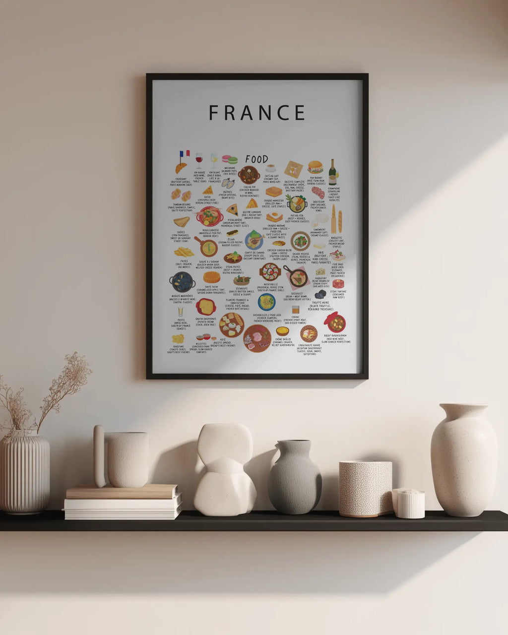 A framed France food poster hangs on a wall above a black shelf styled with neutral ceramic vases, books, and dried florals.
