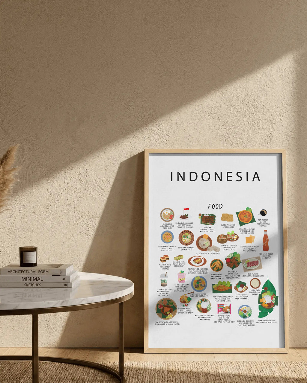 Framed white Indonesia food poster resting on the floor against a textured wall, beside a small marble table holding stacked books and a candle.