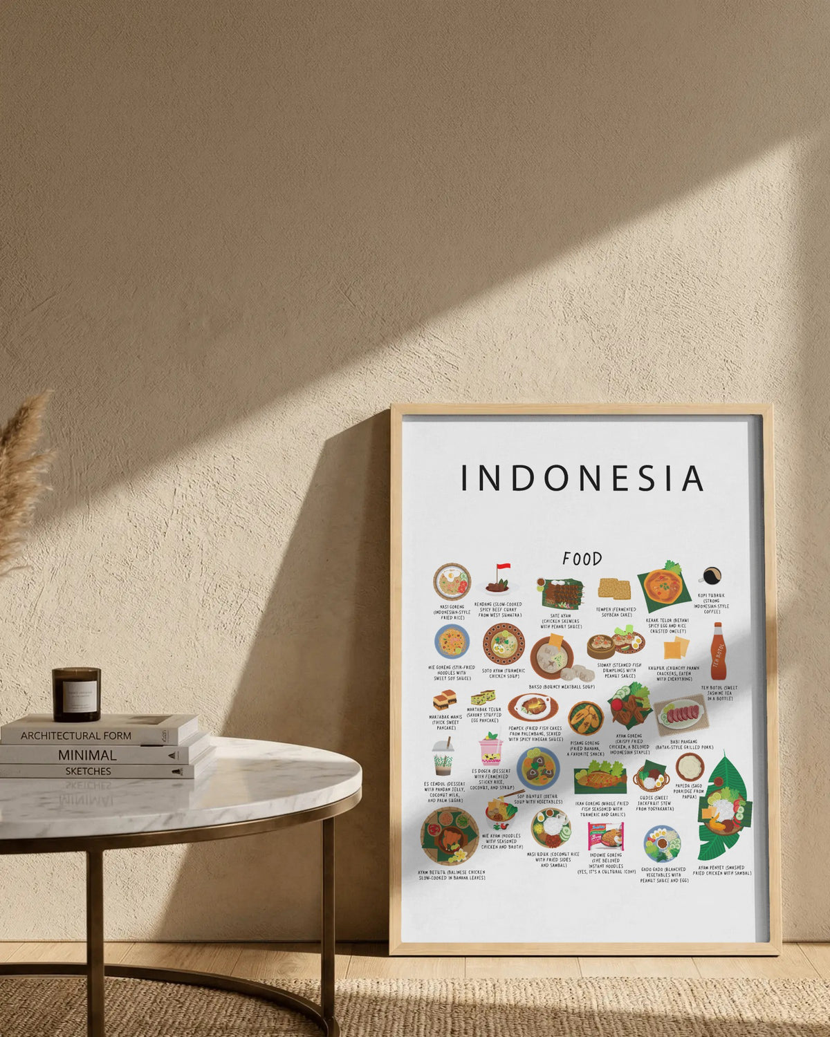 Framed white Indonesia food poster resting on the floor against a textured wall, beside a small marble table holding stacked books and a candle.