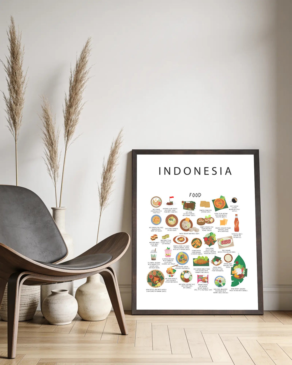 A framed white Indonesia food poster resting on a light wood floor against a white wall, beside a curved wooden lounge chair and dried grass vases.