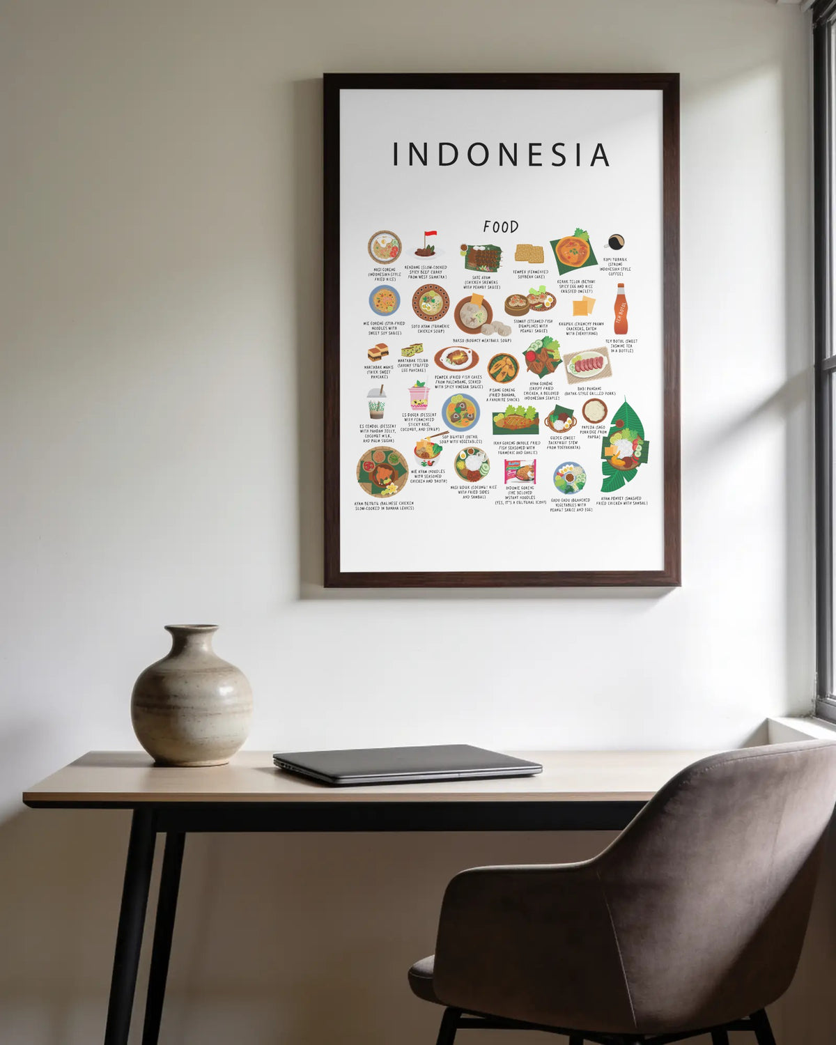 A framed white Indonesia food poster hanging on a white wall above a wooden desk with a ceramic vase, closed laptop, and office chair.