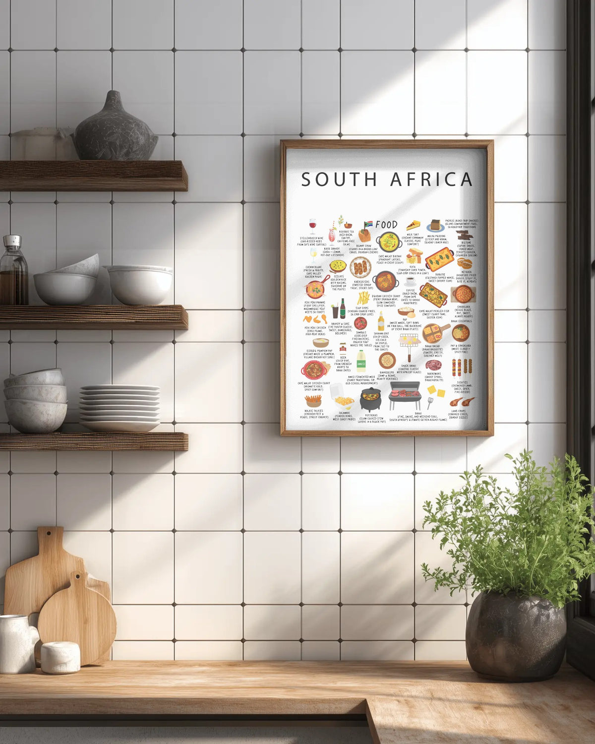 A framed South Africa food poster hangs on a white tiled kitchen wall beside wooden open shelves and above a wooden countertop with a plant.