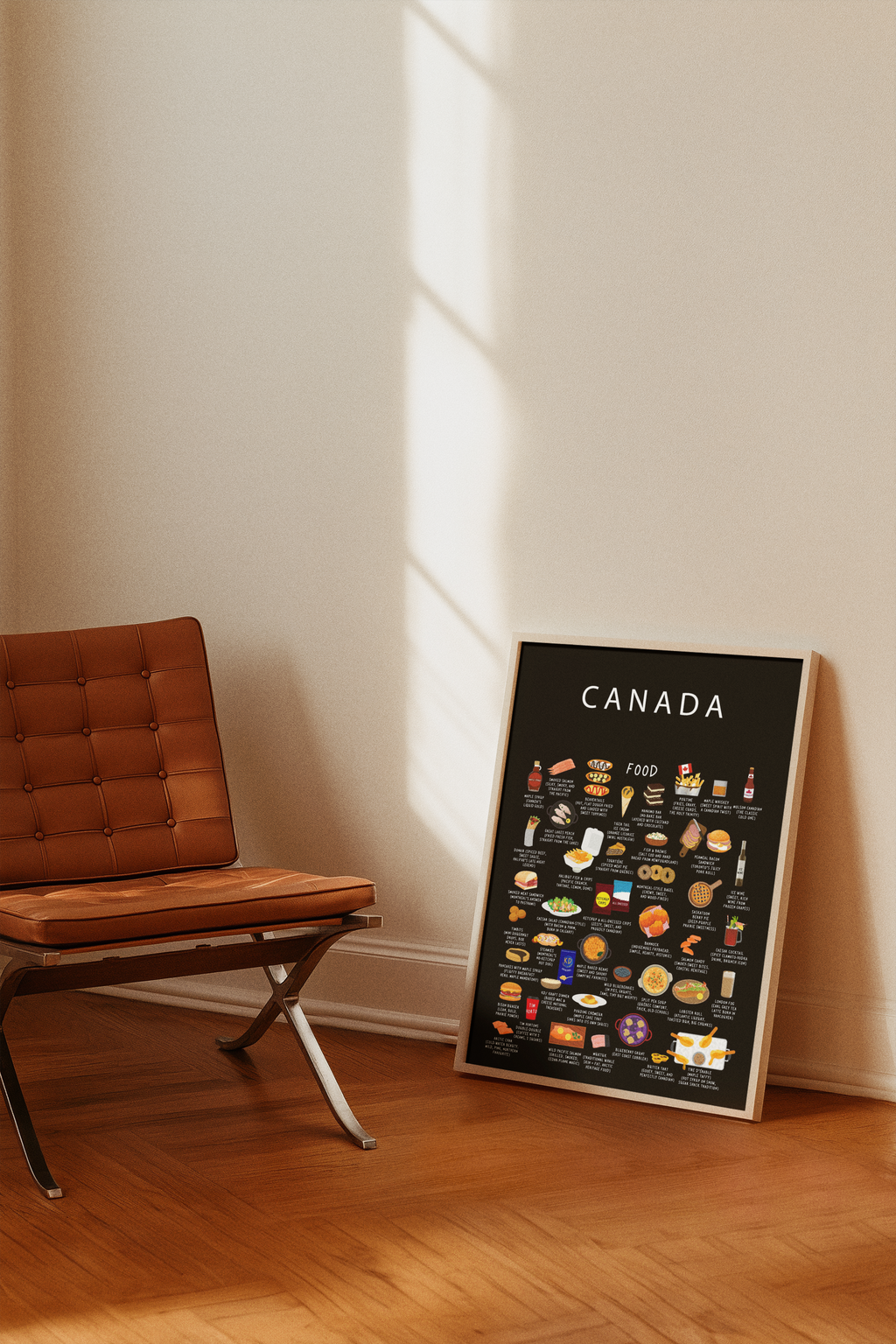 A framed black Canada food poster rests on a wooden floor against a sunlit wall beside a brown leather chair.