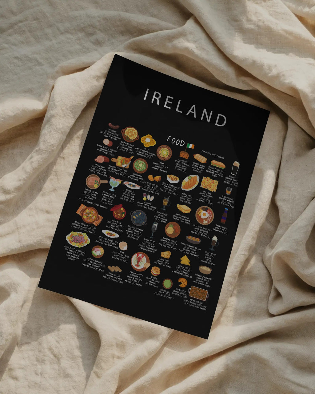A black illustrated Ireland food poster placed flat at an angle on top of textured, draped cream-colored linen.