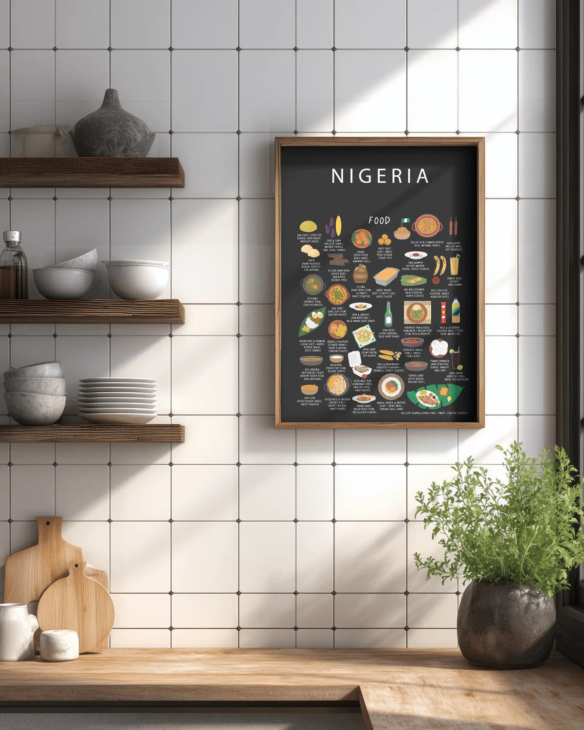 A framed black Nigeria food poster hangs on a white tiled wall in a kitchen beside open shelves with bowls and a potted plant.